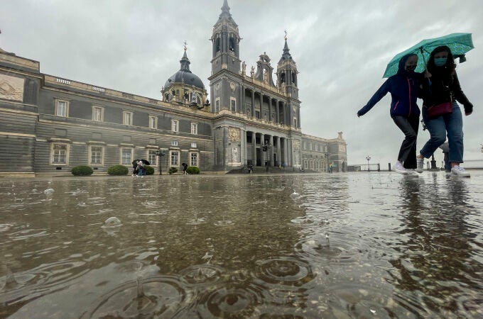 Dos mujeres caminan bajo la lluvia en las inmediaciones de la catedral de la Almudena