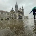 Dos mujeres caminan bajo la lluvia en las inmediaciones de la catedral de la Almudena