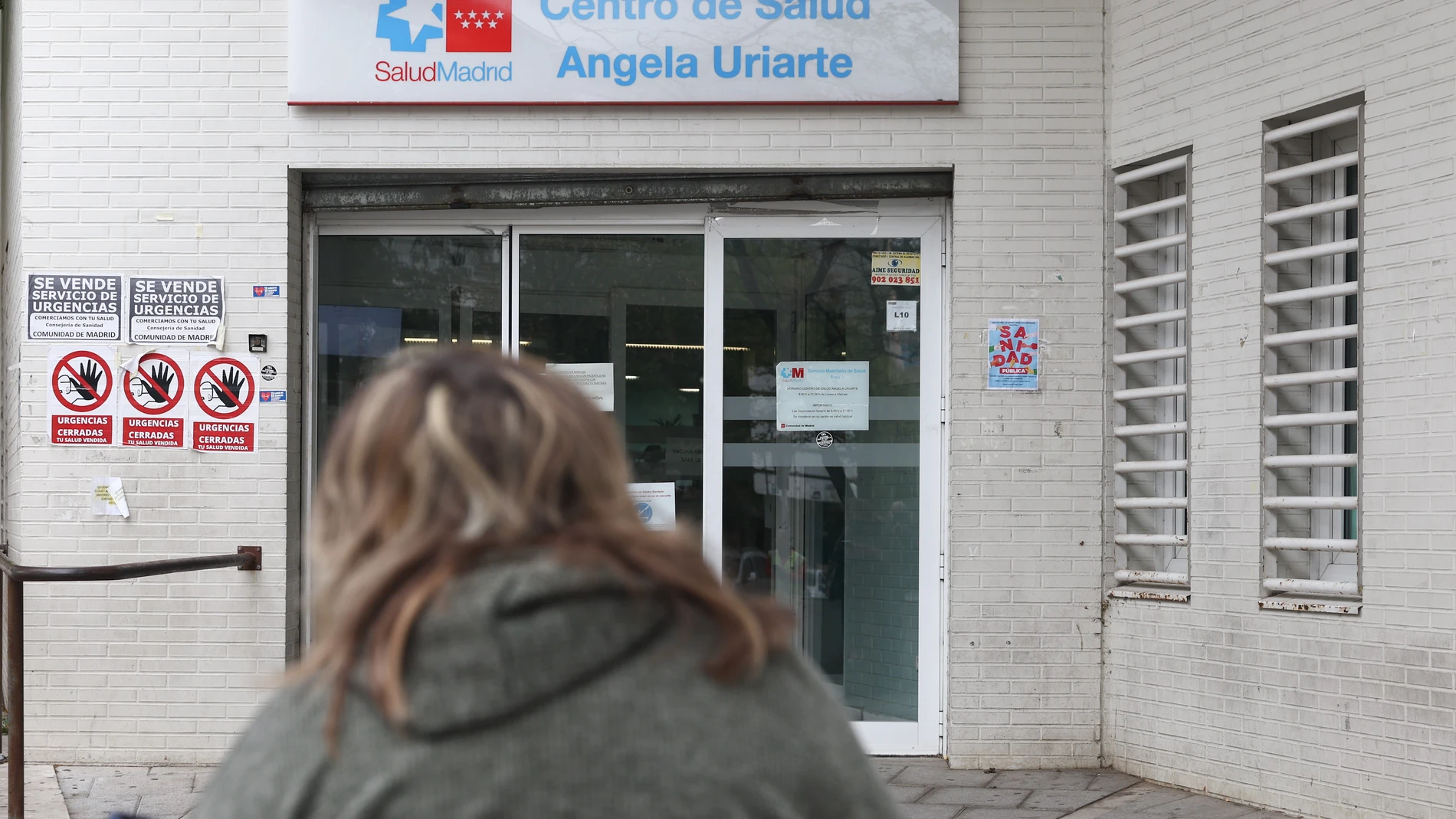 Una mujer llega al Centro de Salud Ángela Uriarte, donde hay carteles de protesta que rezan 'Urgencias Cerradas, tu salud vendida