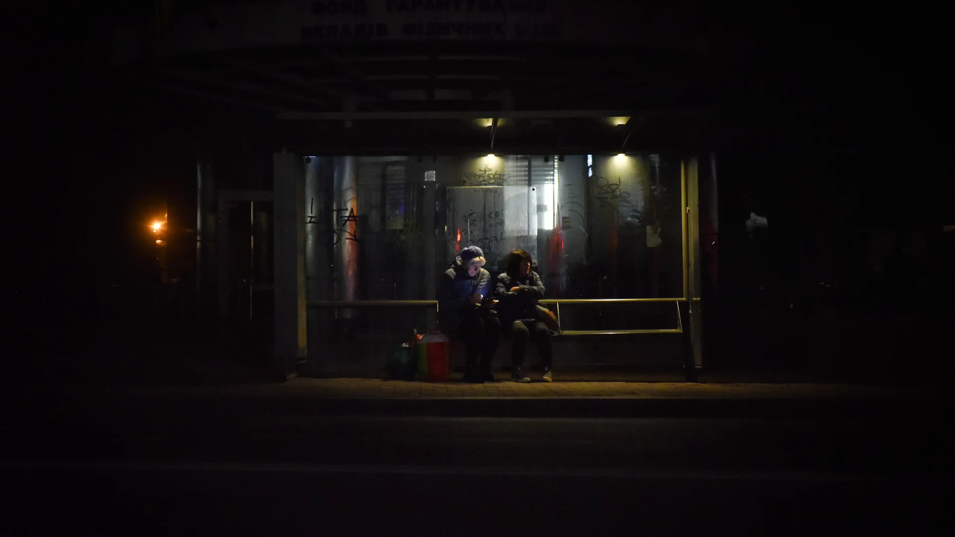 Dos ucranianos sentados en la parada de autobús en la oscuridad este 22 de octubre en Kyiv