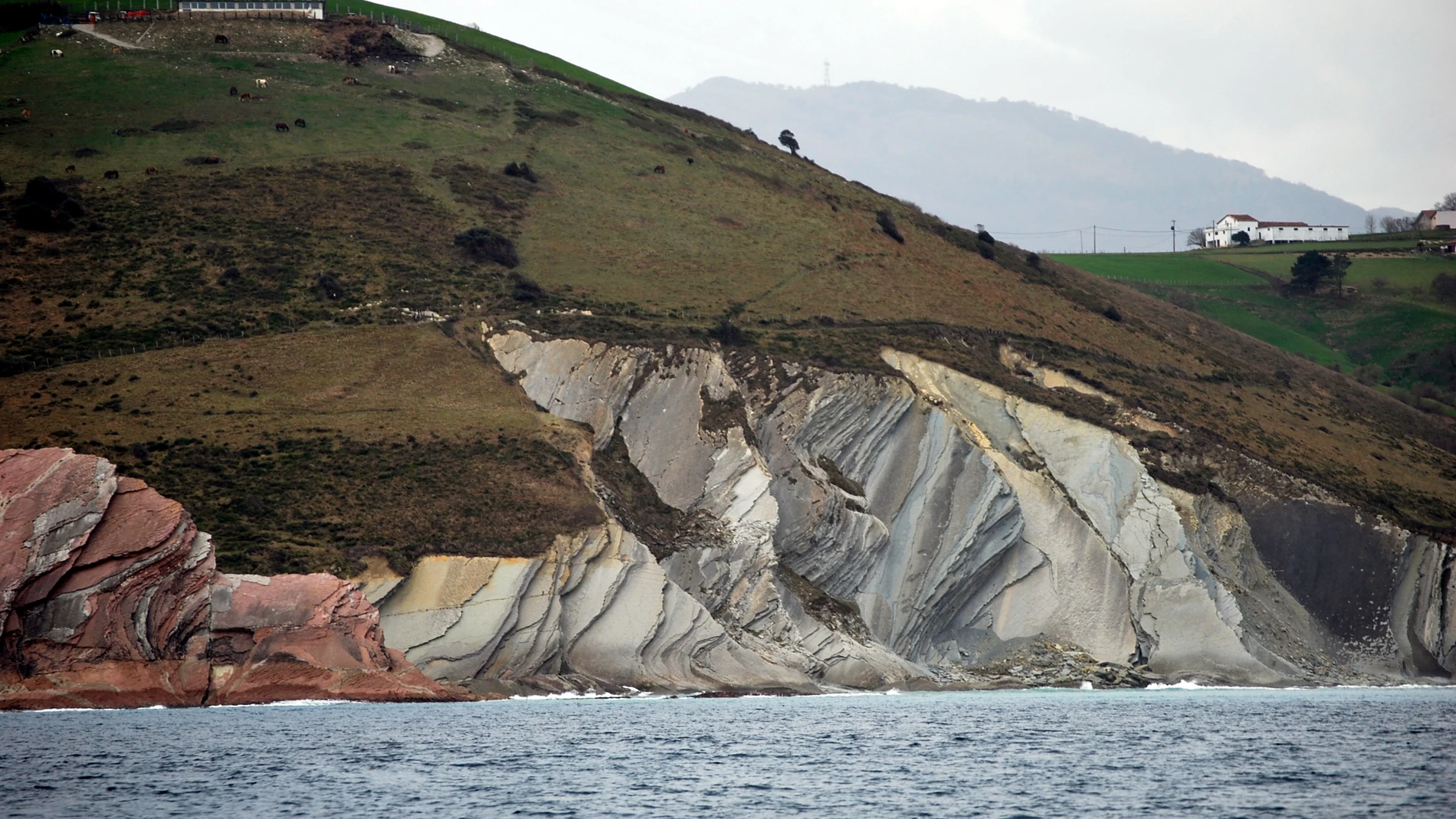 Un acantilado en tonos grises y rojizos frente al mar