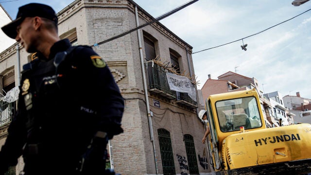 Un agente de Policía Nacional frente a una máquina retroexcavadora durante la demolición del edificio okupado ‘La Higuera’, en el barrio de Tetuán