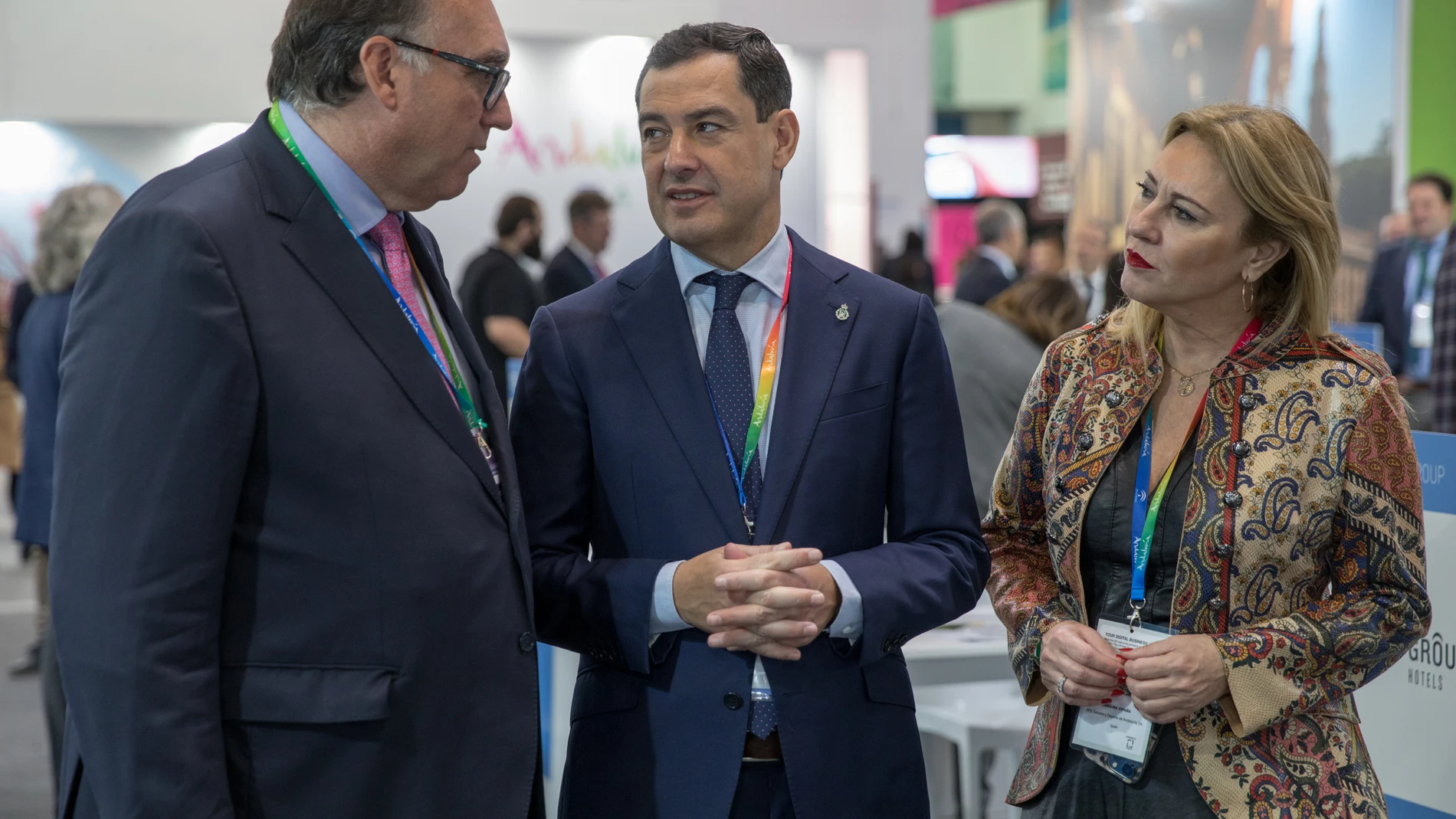 El presidente de la Junta de Andalucía, Juanma Moreno(c), charla con el consejero de Turismo, Arturo Bernal (i), y la consejera de Economía, Carolina España, este lunes en el pabellón andaluz de la WTM de Londres