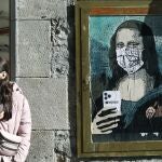 Imagen de un artista callejero que muestra a la Gioconda con mascarilla y móvil