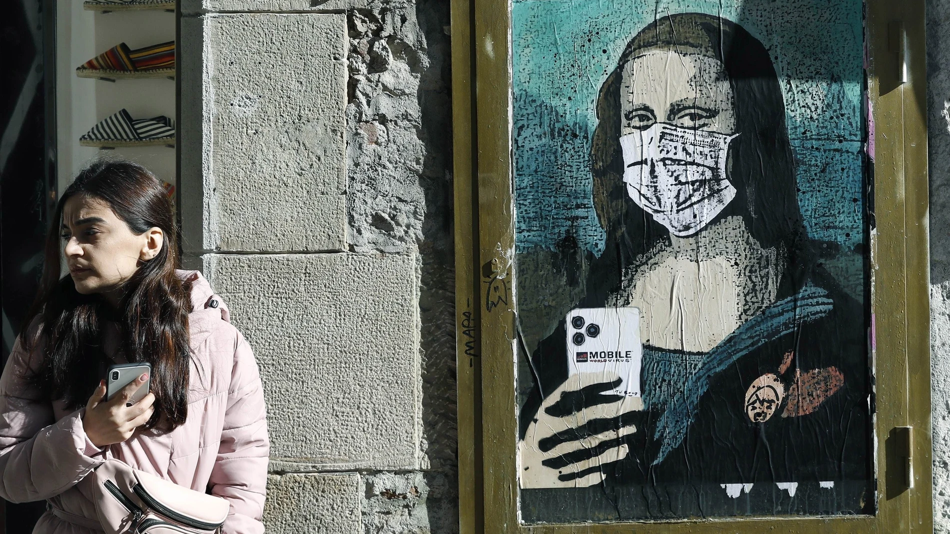 Imagen de un artista callejero que muestra a la Gioconda con mascarilla y móvil