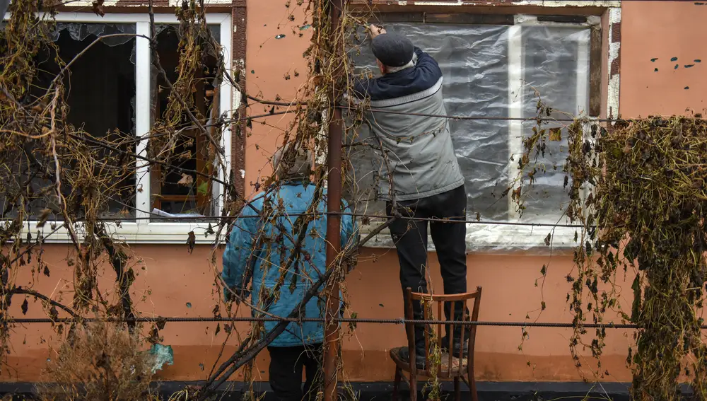 Svitlana y Leonid reparan una ventana de la casa dañada a la que regresaron tras la acción de combate en Posad-Pokrovske