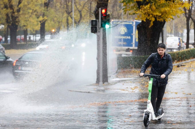 Un hombre usa un patinete eléctrico bajo la lluvia en Madrid