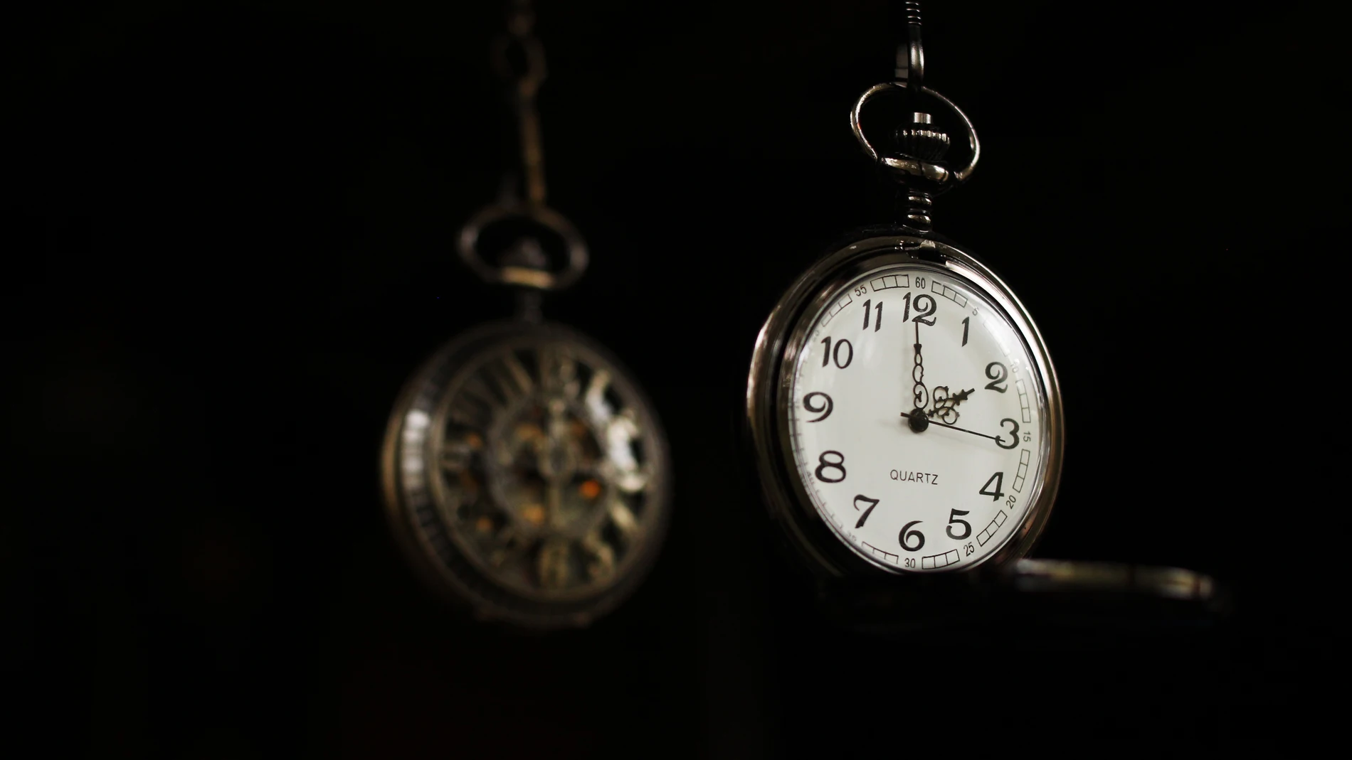 Un reloj de bolsillo que marca las dos en punto, con su reflejo borroso detrás