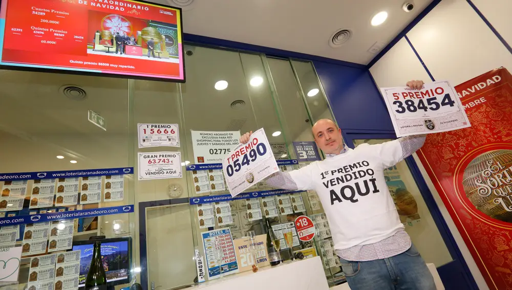 Un empleado de la administración situada en el Centro Comercial Río Shopping posa junto con dos números ganadores mientras celebran que han vendido parte del número 5490 correspondiente al 'Gordo'