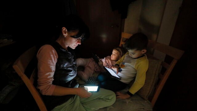 Una madre con sus hijos sentados en el oscuro pasillo de su piso mientras se corta la electricidad durante una alarma antiaérea en Kyiv