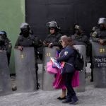 Mujeres caminan junto a los antidisturbios que custodian las instalaciones policiales donde se mantiene detenido a Luis Fernando Camacho, gobernador de Santa Cruz, en La Paz, Bolivia