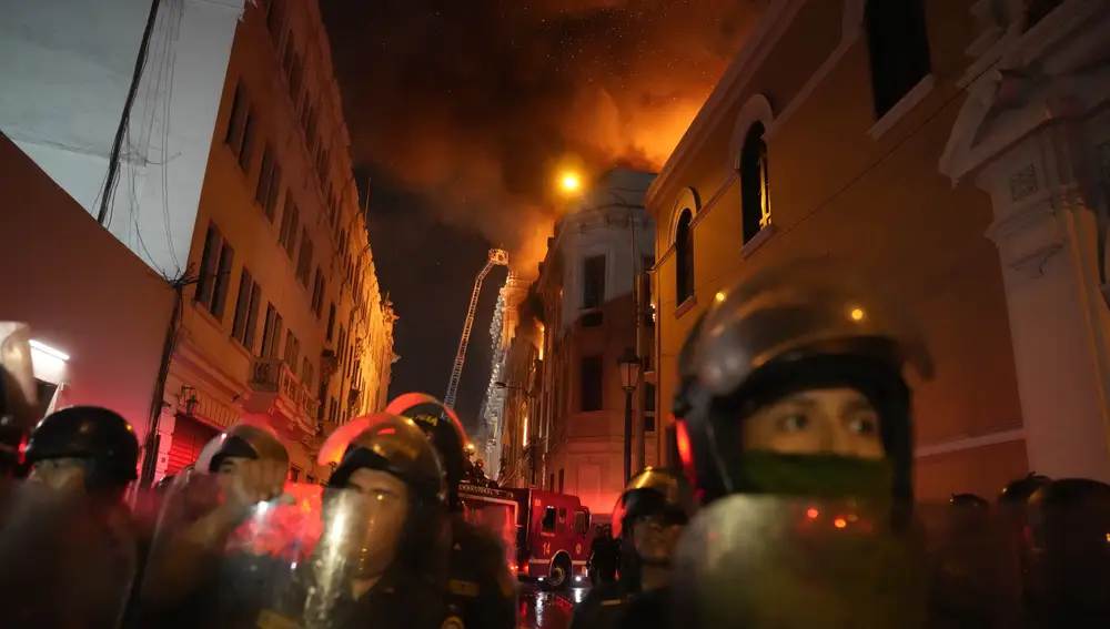 Policías antidisturbios bloquean una calle mientras un edificio arde detrás de ellos tras un día de enfrentamientos con manifestantes antigubernamentales en Lima