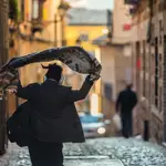 Una persona se echa una prenda de abrigo sobre los hombros mientras camina por una calle de Toledo