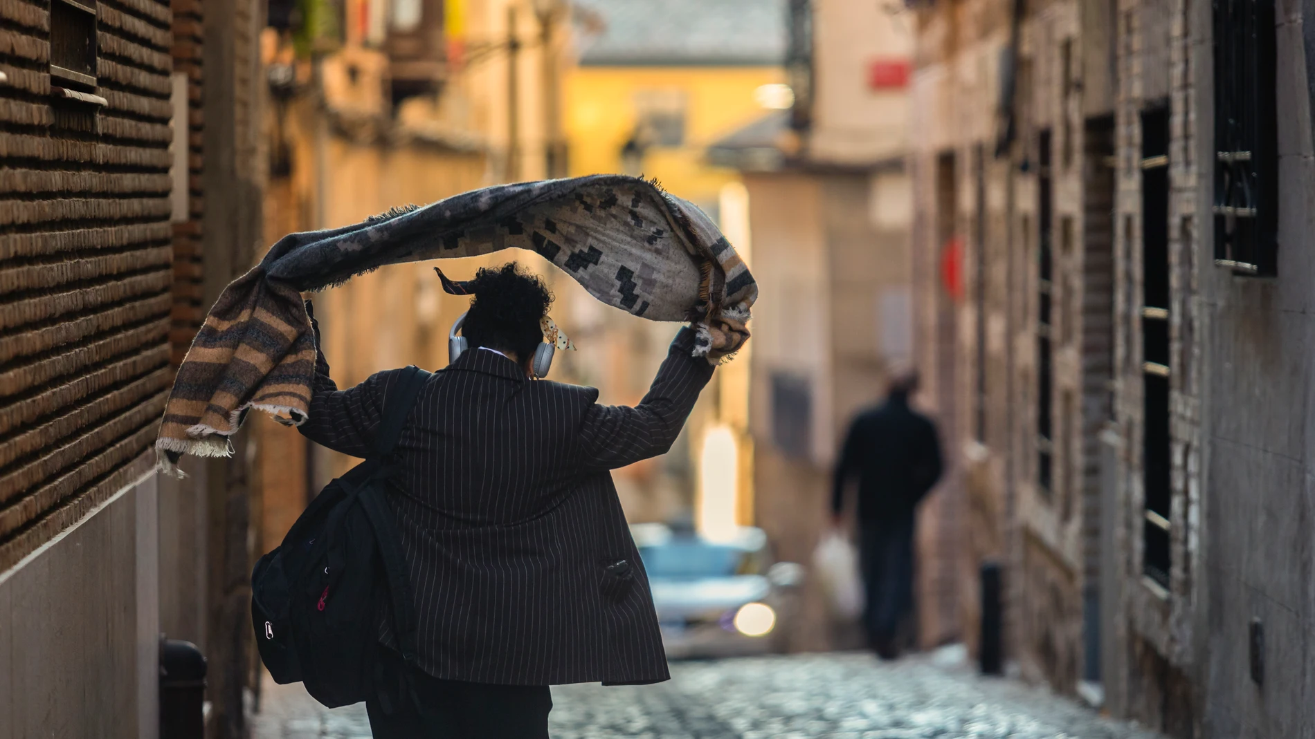 Una persona se echa una prenda de abrigo sobre los hombros mientras camina por una calle de Toledo