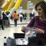 Una mujer deposita una bolsa de plástico en la que ha metido maquillaje, crema y geles en una bandeja antes de pasar por el control de seguridad del aeropuerto Madrid-Barajas. 
