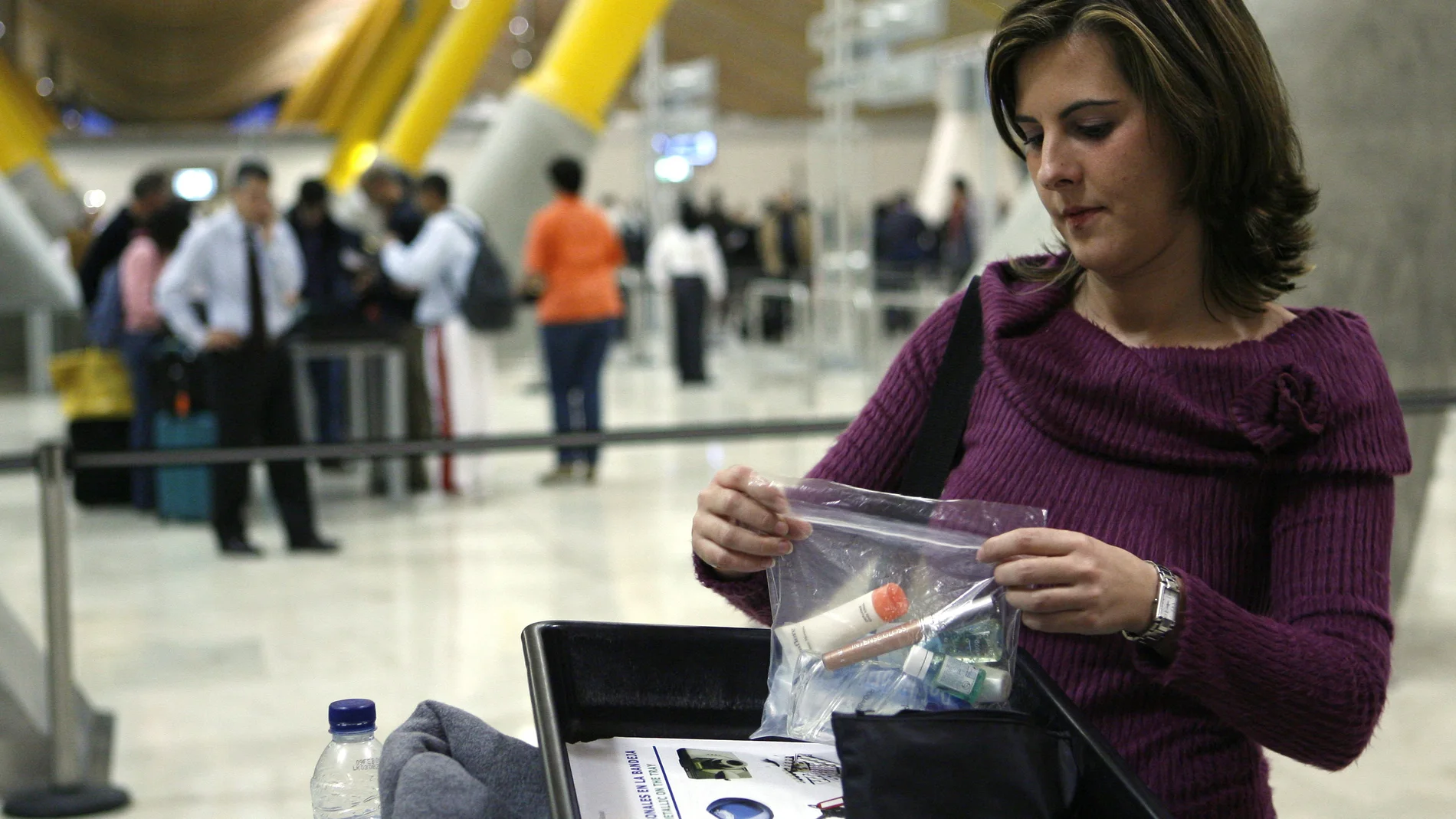 Una mujer deposita una bolsa de plástico en la que ha metido maquillaje, crema y geles en una bandeja antes de pasar por el control de seguridad del aeropuerto Madrid-Barajas.