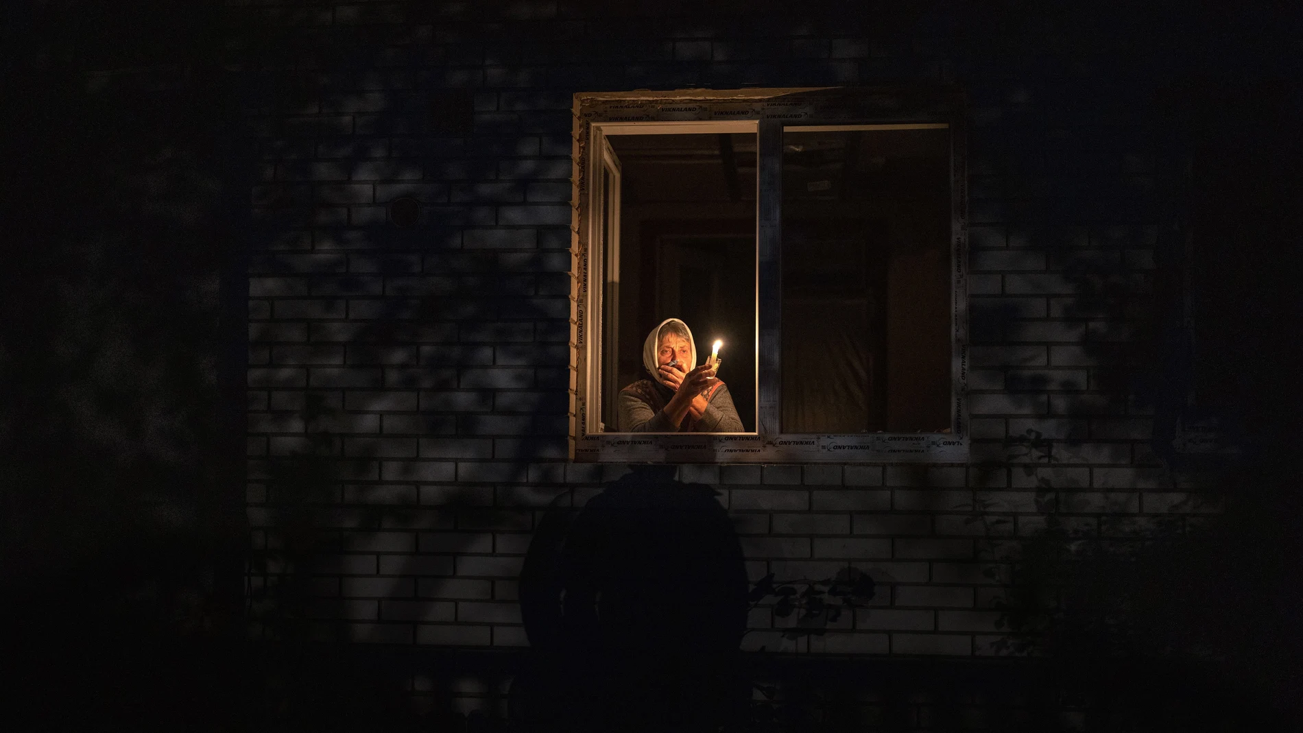 Catherine, 70, holds a candle in the window of her home during a power outage in Borodyanka, Kyiv region, Ukraine