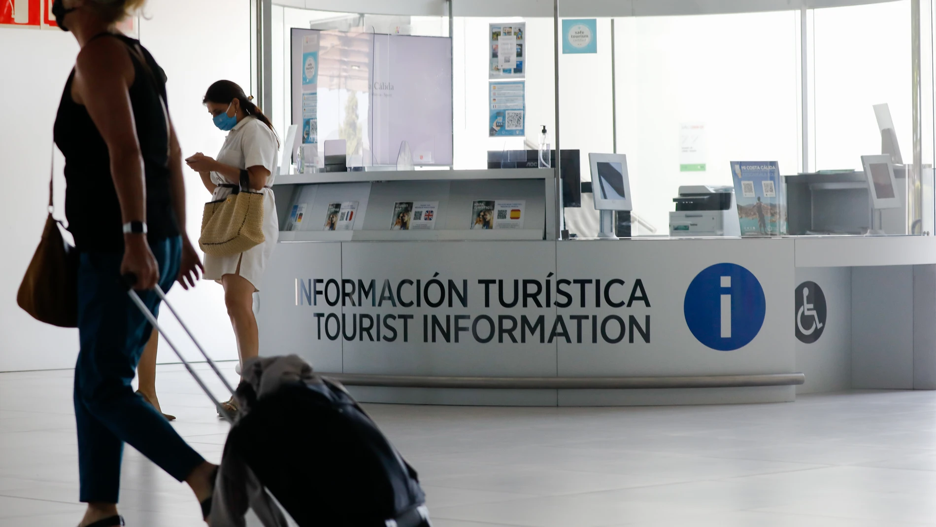 Varias personas pasan por delante de la Oficina de Turismo del Aeropuerto Internacional de la Región de Murcia