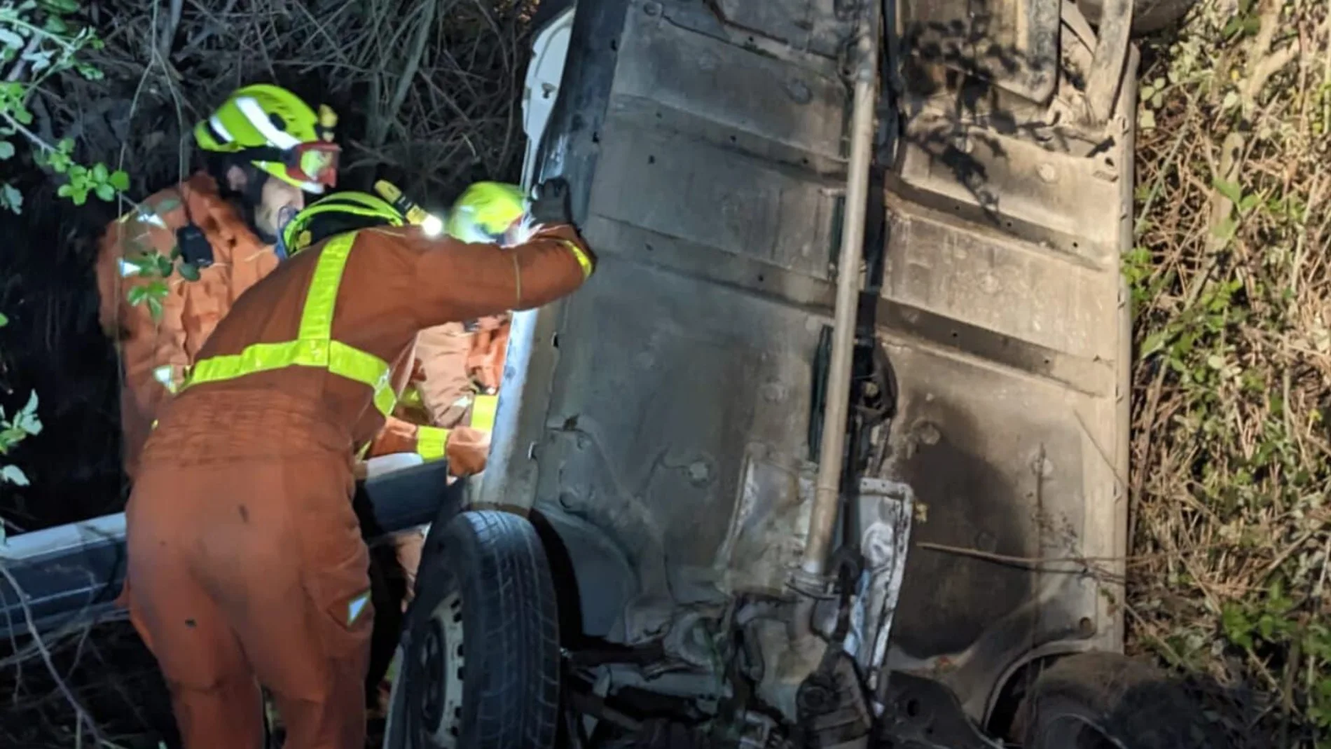 Los bomberos tratan de liberar al hombre cuyo coche cayó al barranco