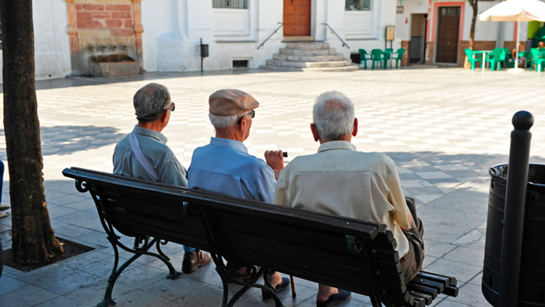Tres hombres mayores sentados en la plaza de un pueblo