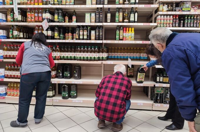 Varias personas compran aceite en un supermercado de Madrid, donde algunas estanterías permanecen vacías a causa de la huelga indefinida de transporte.