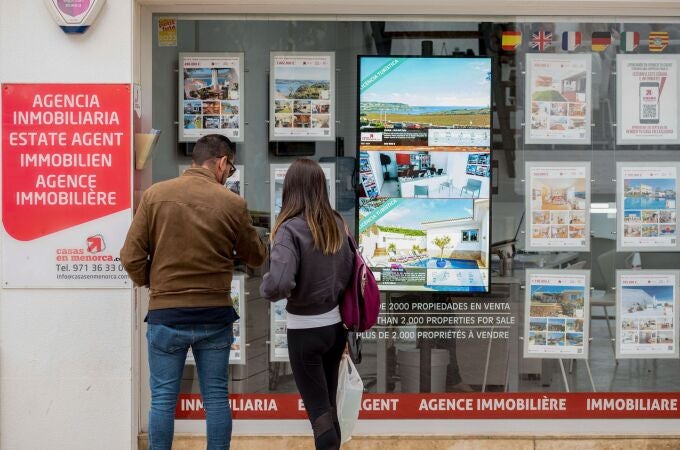  Una pareja se detiene a observar las propiedades en venta anunciadas en el escaparate de una agencia inmobiliaria de Menorca.