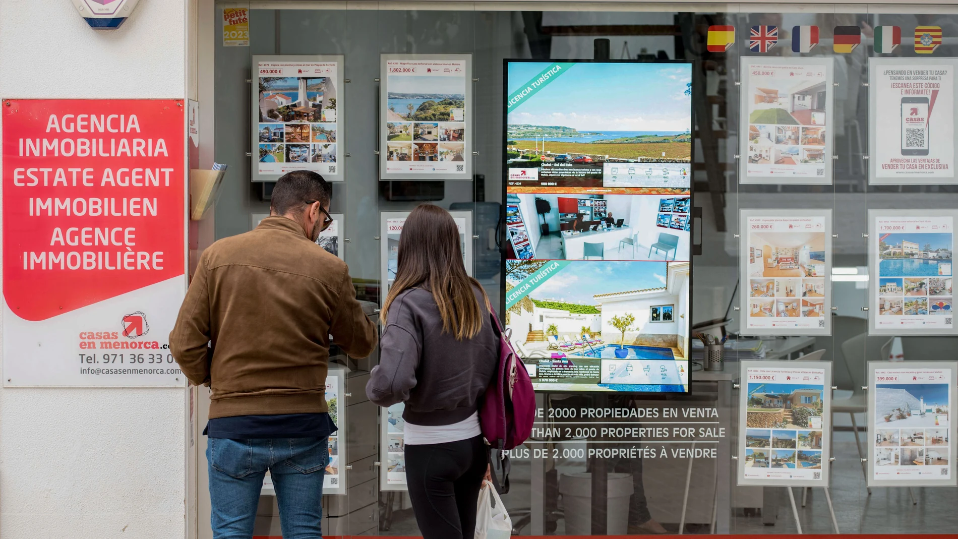  Una pareja se detiene a observar las propiedades en venta anunciadas en el escaparate de una agencia inmobiliaria de Menorca.