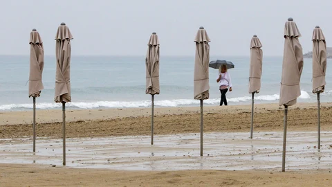 Una persona pasea bajo la lluvia por la playa de El Postiguet de Alicante