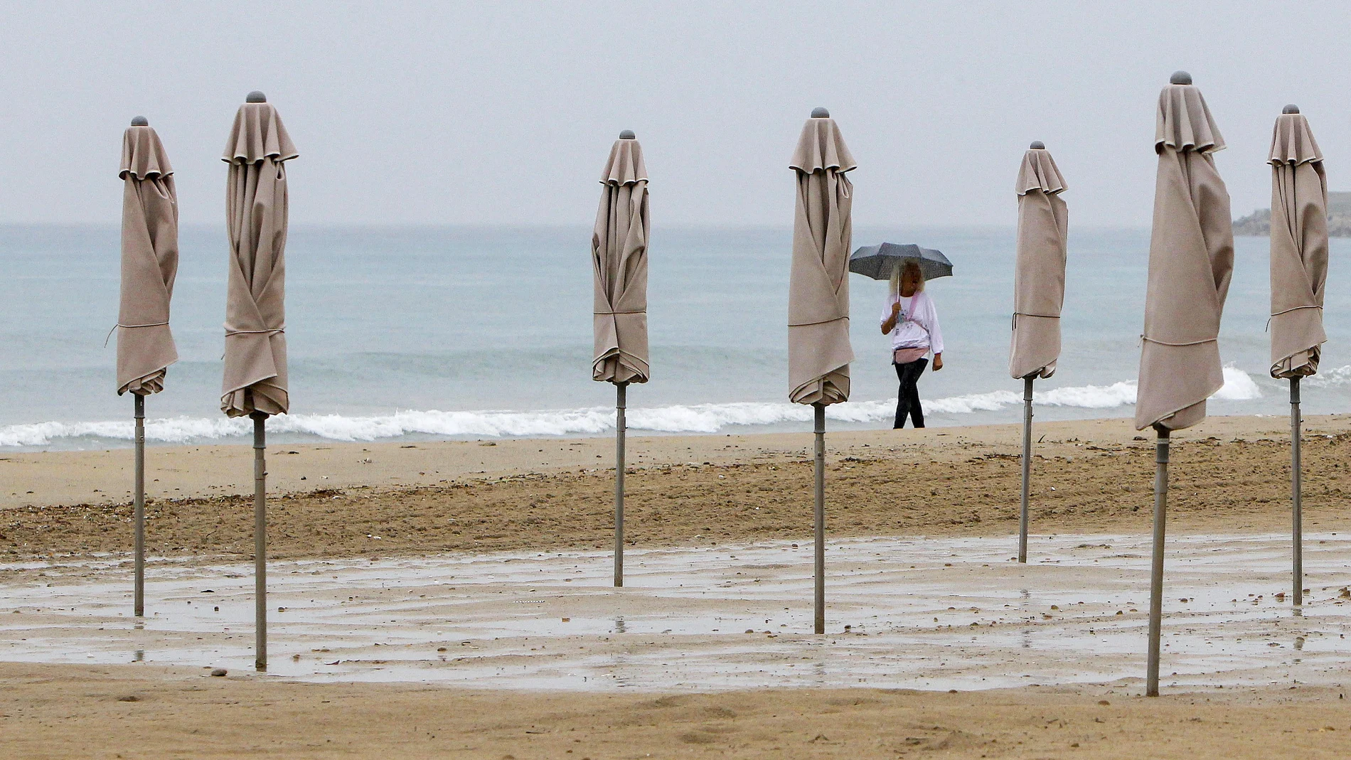 Una persona pasea bajo la lluvia por la playa de El Postiguet de Alicante 