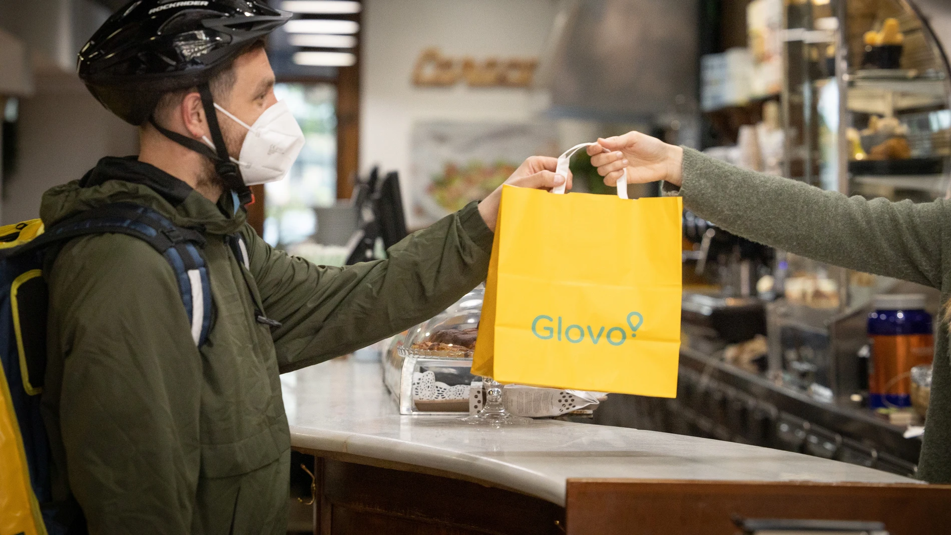 Repartidor de Glovo! haciendo la entrega de un pedido en una de sus bolsas de papel