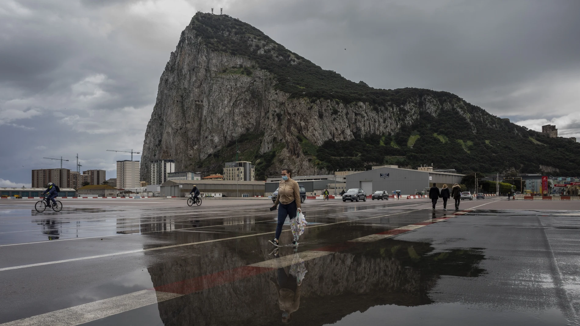 People cross the Gibraltar airport runway towards the border crossing with Spain, backdropped by the Gibraltar rock, in Gibraltar, Friday, March 5, 2021.