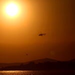 Un sol abrasador en Grecia mientras un helicóptero se dispone a cargar agua contra un incendio