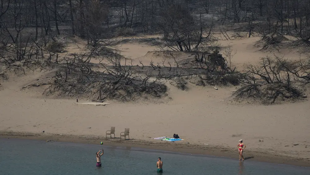 Dos bañistas juegan con una pelota frente a un bosque quemado en una playa cerca de la aldea de Gennadi en Rodas, una turística isla griega en el mar Egeo, al sureste de Grecia, hoy jueves 27 de julio de 2023