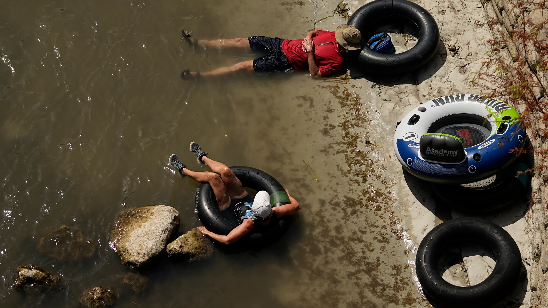 A couple take a break on the banks of the Comal River, Wednesday, July 26, 2023, in New Braunfels, Texas, as the area continues to feel the effects of triple-digit temperatures. (AP Photo/Eric Gay)