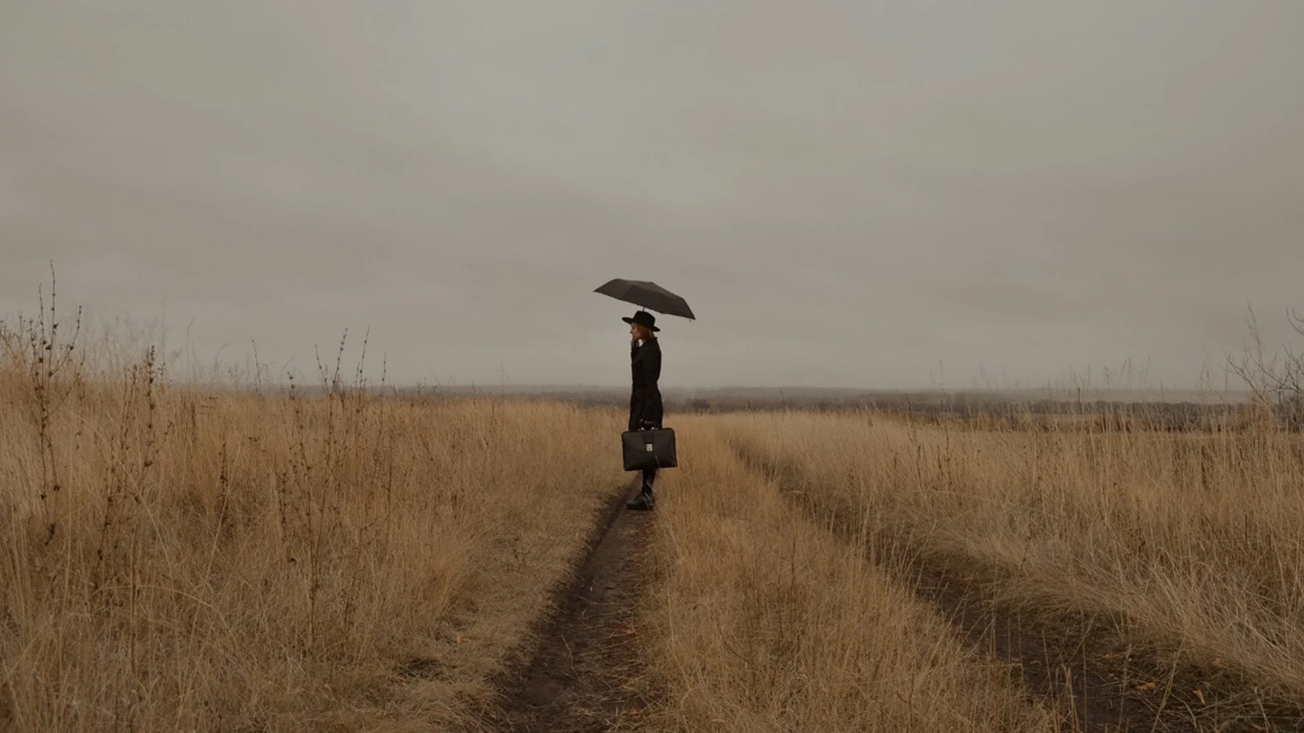Mujer de negro en medio de un campo bajo un paraguas 