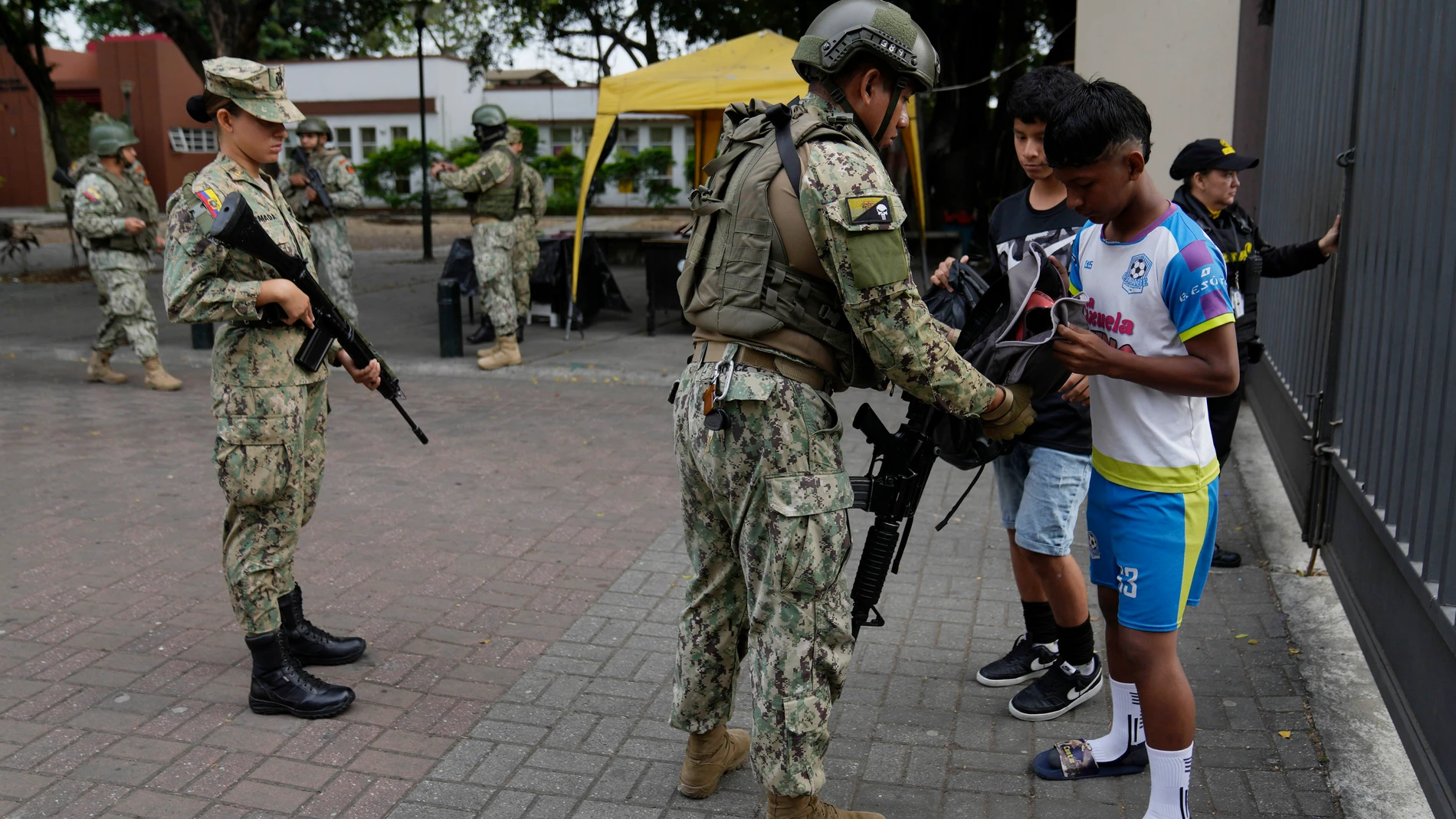 Soldiers search the backpacks of students on school grounds in downtown Guayaquil, Ecuador, Friday, Aug. 18, 2023. Ecuadorians will choose a new president Sunday, less than two weeks after the South American country was shaken by the assassination of one of the candidates(AP Photo/Martin Mejia)