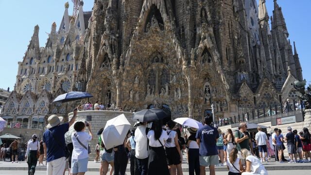 Varios turistas equipados con sombrillas visitan la Sagrada Familia, en Barcelona.