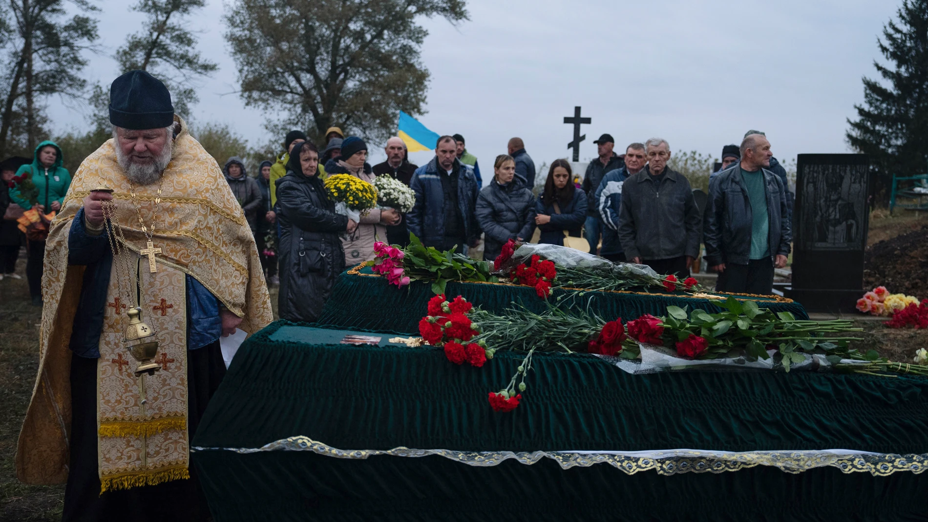 A priest conducts a service by the coffins of Tetiana Androsovych, 60, and Mykola Androsovych, 63, killed by a rocket strike, at a graveyard in the village of Hroza, near Kharkiv, Ukraine, Saturday, Oct. 7, 2023. The Ukrainian village of Hroza has been plunged into mourning by a Russian rocket strike on a village store and cafe that killed more than 50 people on Thursday, Oct. 5. (AP Photo/Alex Babenko)