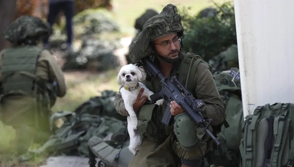 An Israeli soldier carries a dog as they take position next to Kfar Aza kibbutz near the border with Gaza, 10 October 2023.