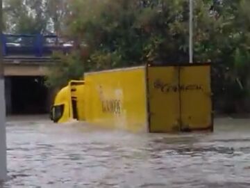 Un repartidor de Correos intenta cruzar una zona inundada con el camión en Madrid