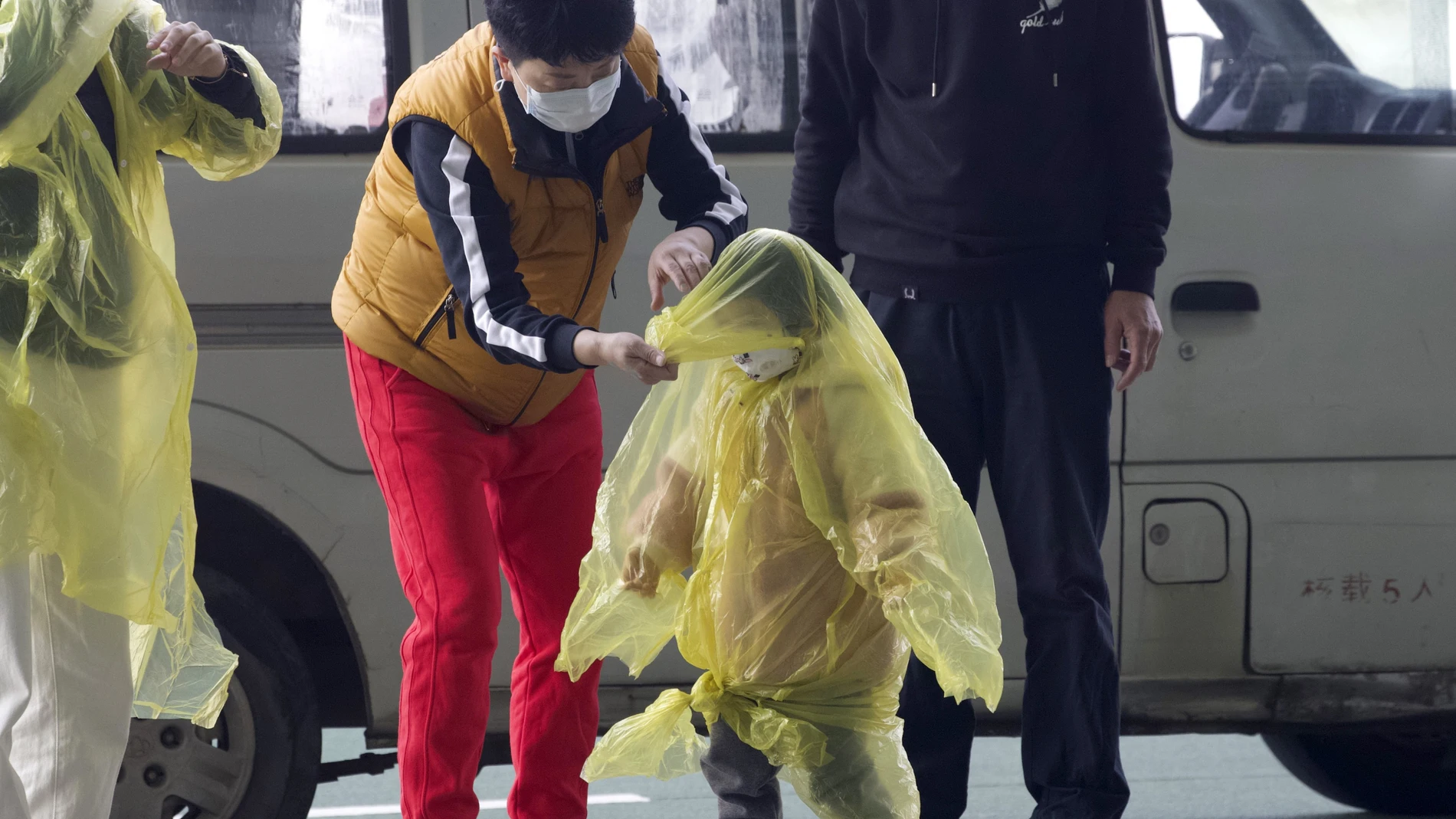 Una mujer intenta proteger de la covid a un niño con un impermeable en Wuhan en abril de 2020