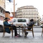 Imagen de un adulto y un niño viendo el teléfono movil en una terraza de Madrid.