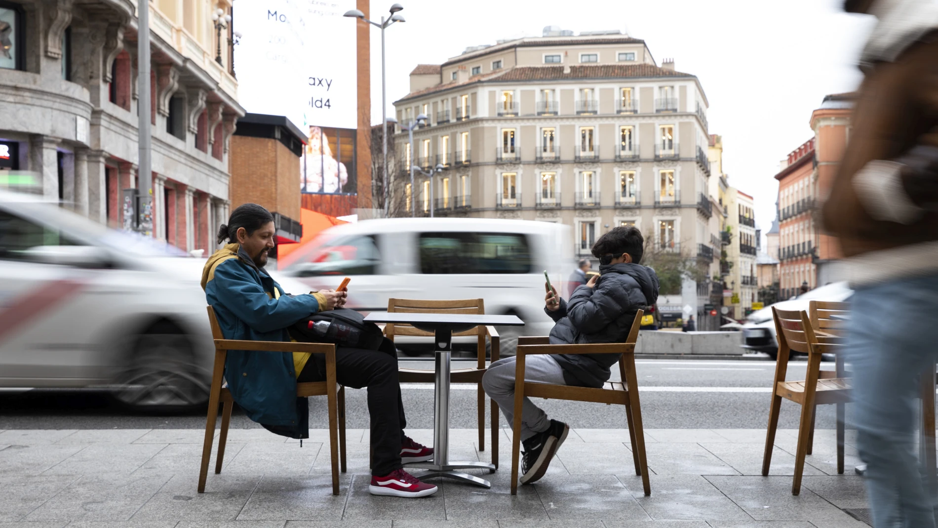 Imagen de un adulto y un niño viendo el teléfono movil en una terraza de Madrid.