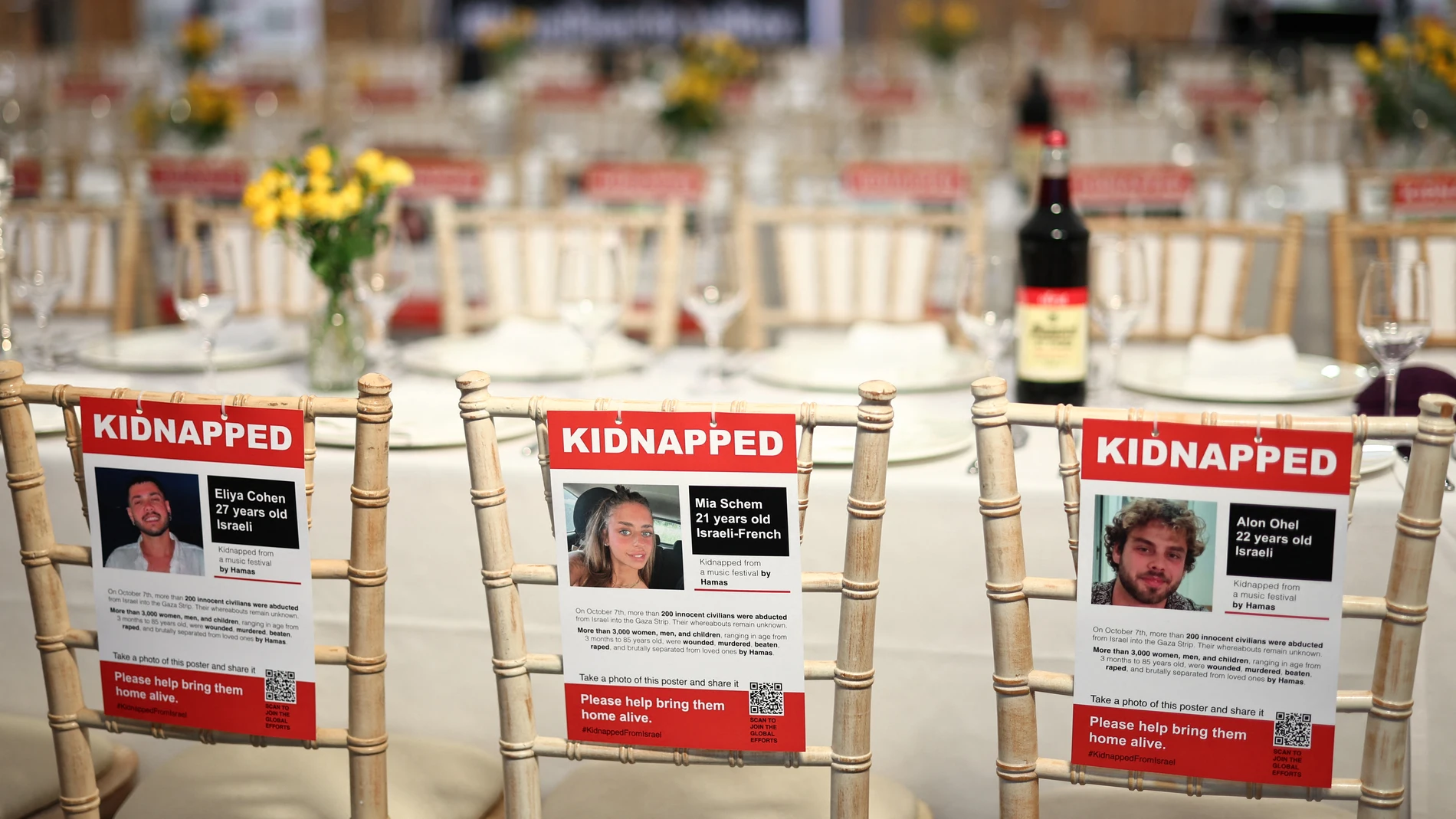 Carteles de tres de los secuestrados, la israelí Eliya Cohen, la franco-israelí Mia Schem y el israelí Alon Ohel se ven pegados a los respaldos de las sillas, en los lugares vacíos dispuestos para los 220 rehenes en una mesa de "Shabat" en la JW3 Piazza en el norte de Londres el 27 de octubre de 2023.