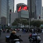 Residents past near an office and retail district with a screen showing the Chinese national flag in Beijing.