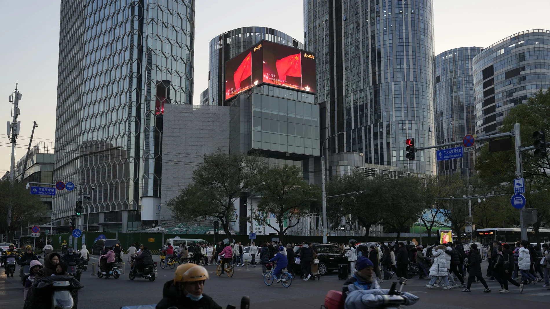 Residents past near an office and retail district with a screen showing the Chinese national flag in Beijing.
