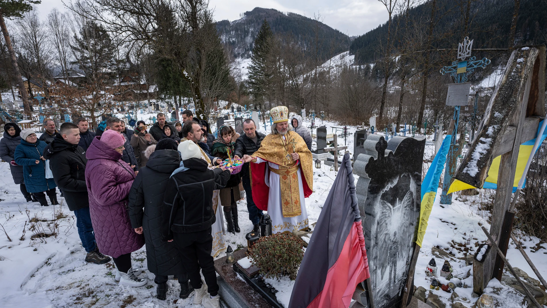 Priest Ivan Rybaruk prays with the family of fallen Ukrainian soldier Victor Ivanov at the cemetery during Christmas celebration in Kryvorivnia village, Ukraine, Sunday, Dec. 24, 2023. Ivanov was killed by Russian armed forces near Bakhmut on October 2022. (AP Photo/Evgeniy Maloletka)