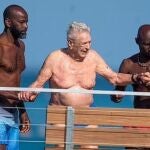 George Soros acompañado de dos hombres que le están ayudando