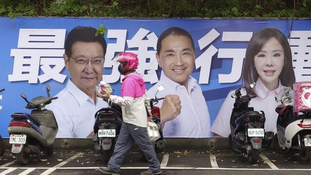 Varias personas pasan junto a un cartel de los candidatos que se presentan a las elecciones presidenciales de Taiwán en Taipéi