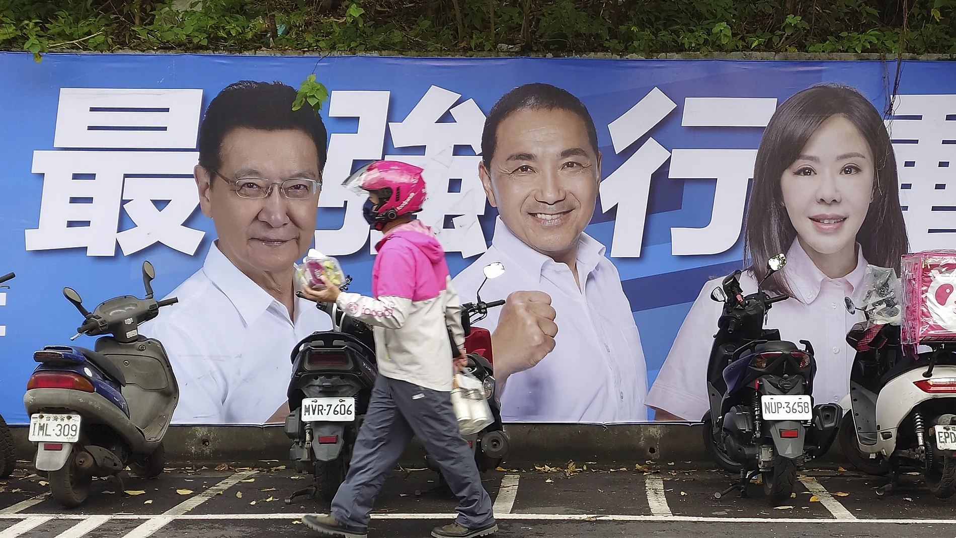 Varias personas pasan junto a un cartel de los candidatos que se presentan a las elecciones presidenciales de Taiwán en Taipéi